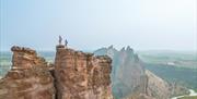 Mountains and green landscape with a mountain ridge with two people stood on top.