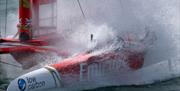 A SailGP catamaran send up sea spray during a race