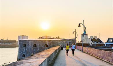 People walking along the fortifications of Old Portsmouth at sunset