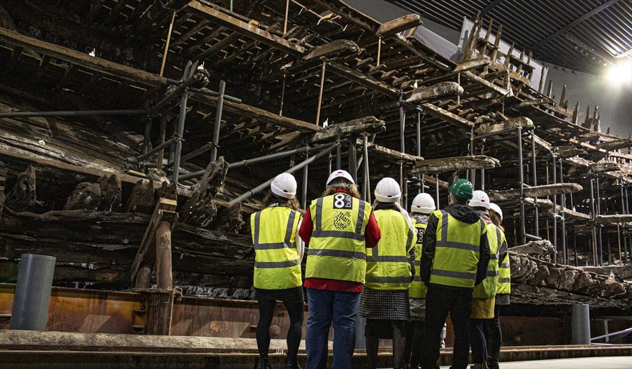 A group of people in high-vis jackets looking up at the salvaged hull of the Mary Rose.