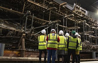 A group of people in high-vis jackets looking up at the salvaged hull of the Mary Rose.
