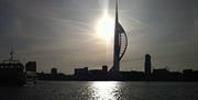 Steely shot of Portsmouth Harbour with a boat in the foreground to the left and the Spinnaker Tower in silhouette