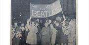 Old photograph showing a group of music fans holding up a home-made banner that reads 'We love The Beatles'