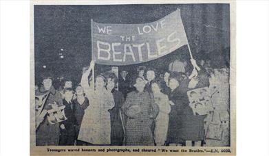 Old photograph showing a group of music fans holding up a home-made banner that reads 'We love The Beatles'