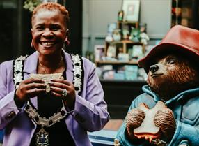 Deputy Mayor of Reading sat on bench with a statue of Paddington Bear eating marmalade sandwiches