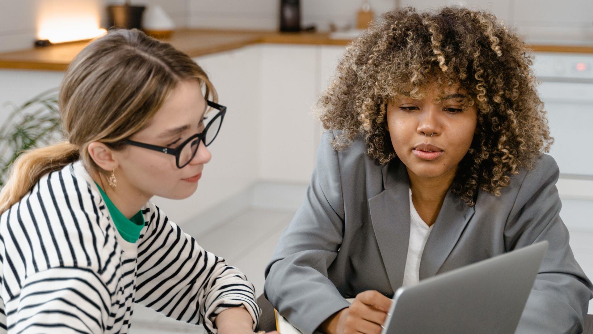 Two casual young business women sat at a table with a laptop