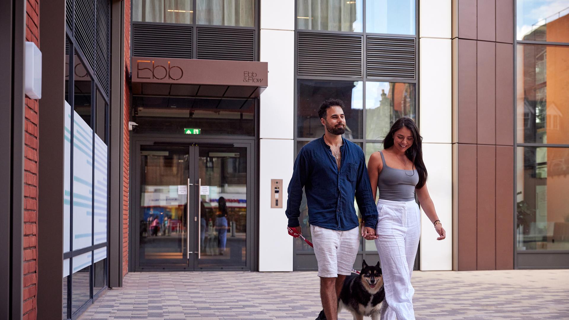 Man and woman walking a dog outside of Ebb apartments