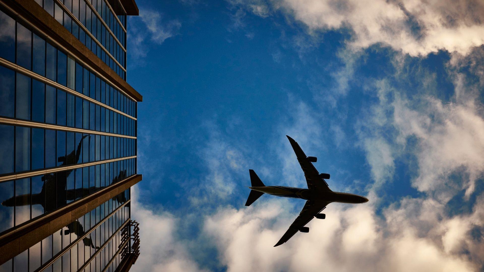 Airplane flying over tall office block in blue sky