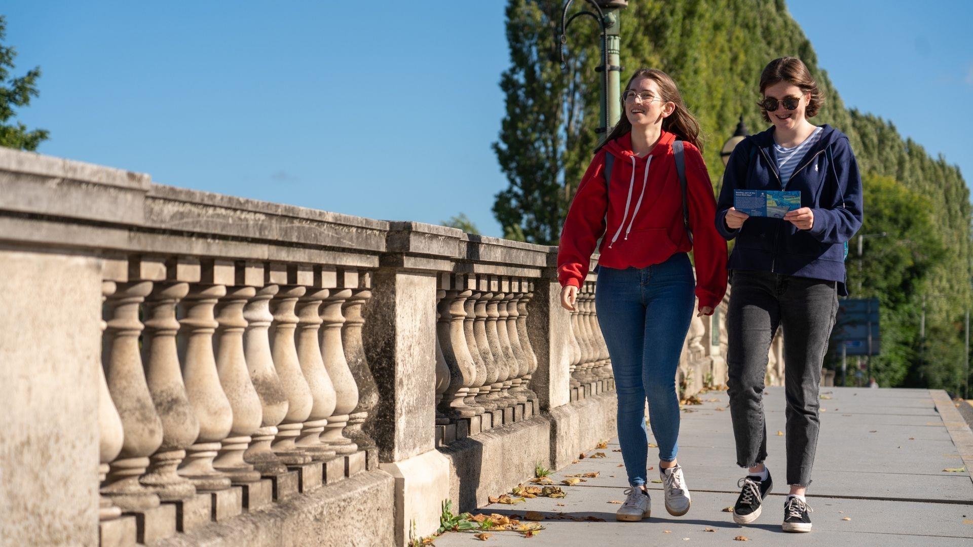 Two young ladies walking over Reading Bridge holding visitor map