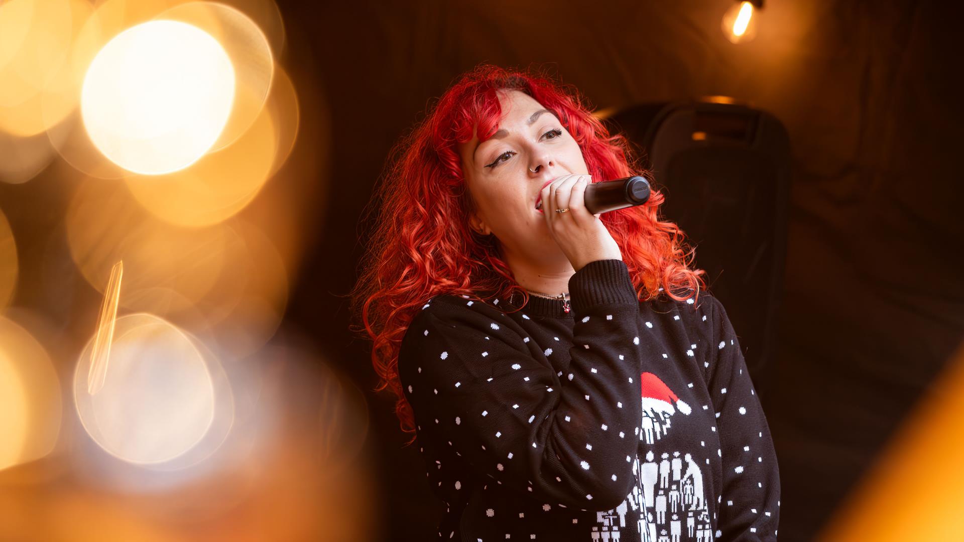 Lady with red curly hair singing live with microphone at Christmas time