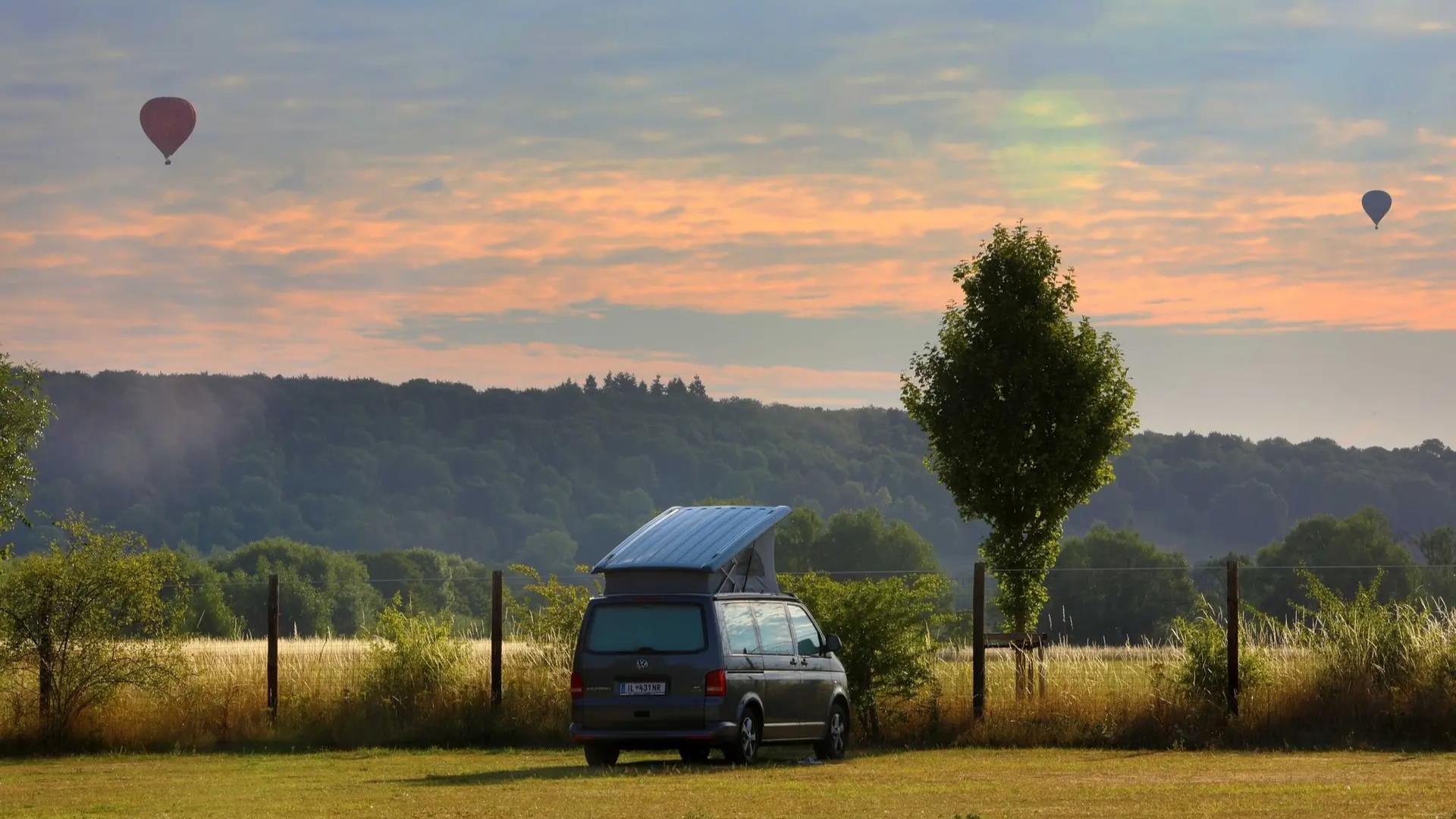 Van with roof box in field with hot air balloons in distance