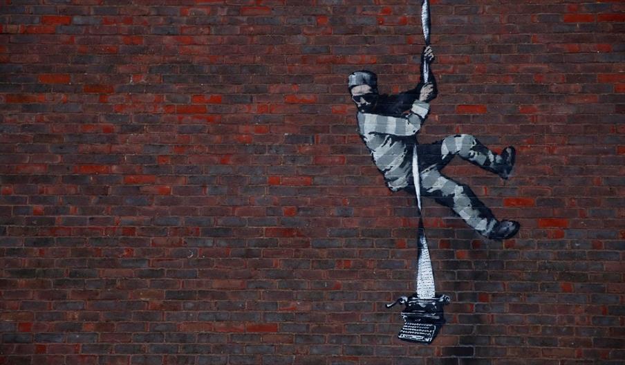 Spraypainted artwork of a prisoner climbing down the wall on a reem of paper attached to a typewriter.