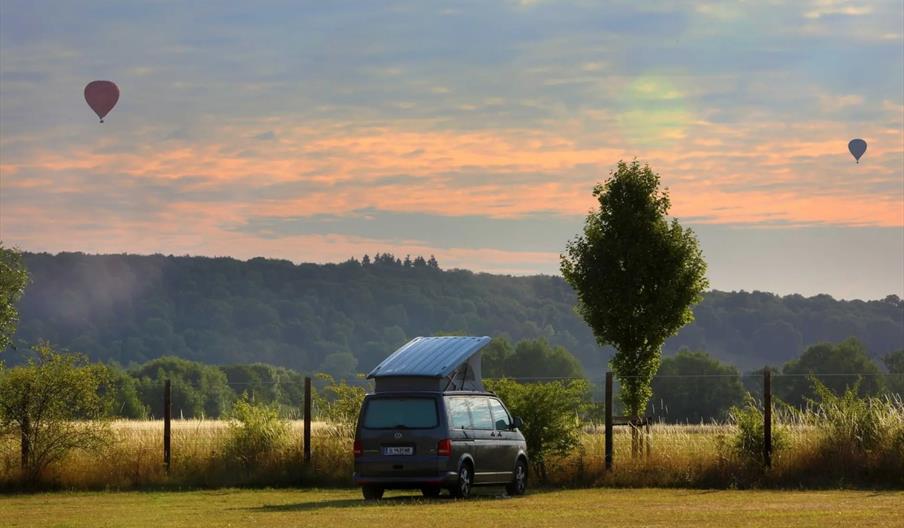 Van with roofbox in front of a sunset and hot air balloons