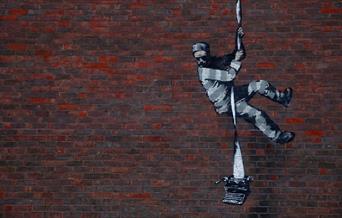 Spraypainted artwork of a prisoner climbing down the wall on a reem of paper attached to a typewriter.
