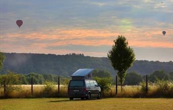 Van with roofbox in front of a sunset and hot air balloons