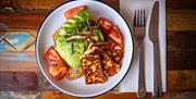 Halloumi, avocado, tomatoes and toast on a plate beside a knife and fork