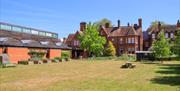 A large lawn with picnic benches and shepherds hut, bordered by the modern museum building and Victorian brick building