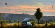 Van with roofbox in front of a sunset and hot air balloons
