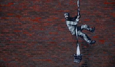 Spraypainted artwork of a prisoner climbing down the wall on a reem of paper attached to a typewriter.