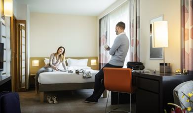 A couple talking in a hotel bedroom.
