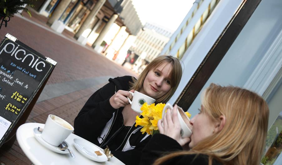 2 girls drinking coffee outside cafe