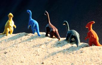 A line of toy dinosaurs in the sand.