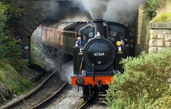 A steam train billowing smoke as it clears a tunnel.