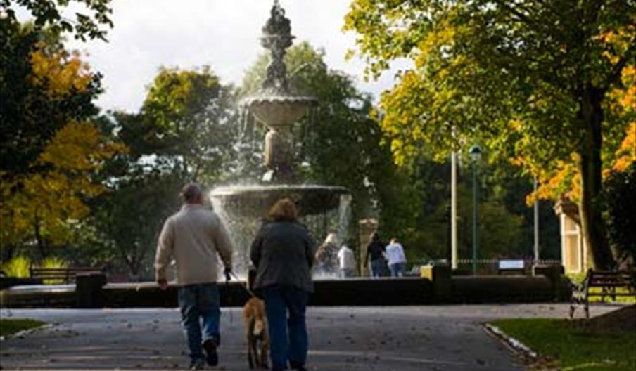 A family at a fountain in Queen's Park on a sunny day.