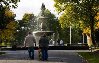 A family at a fountain in Queen's Park on a sunny day.