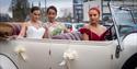 A bride and bridesmaids posing in an open-topped car.