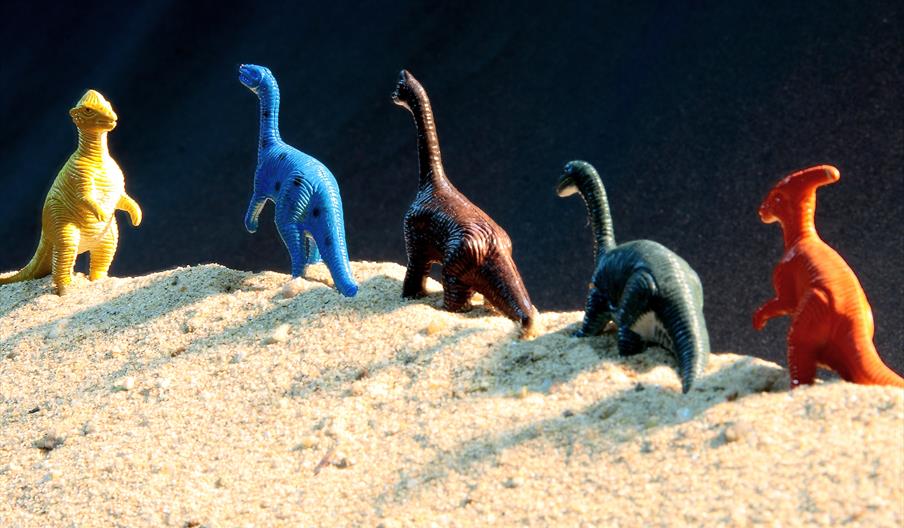 A line of toy dinosaurs in the sand.