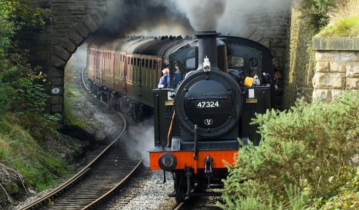 A steam train billowing smoke as it clears a tunnel.