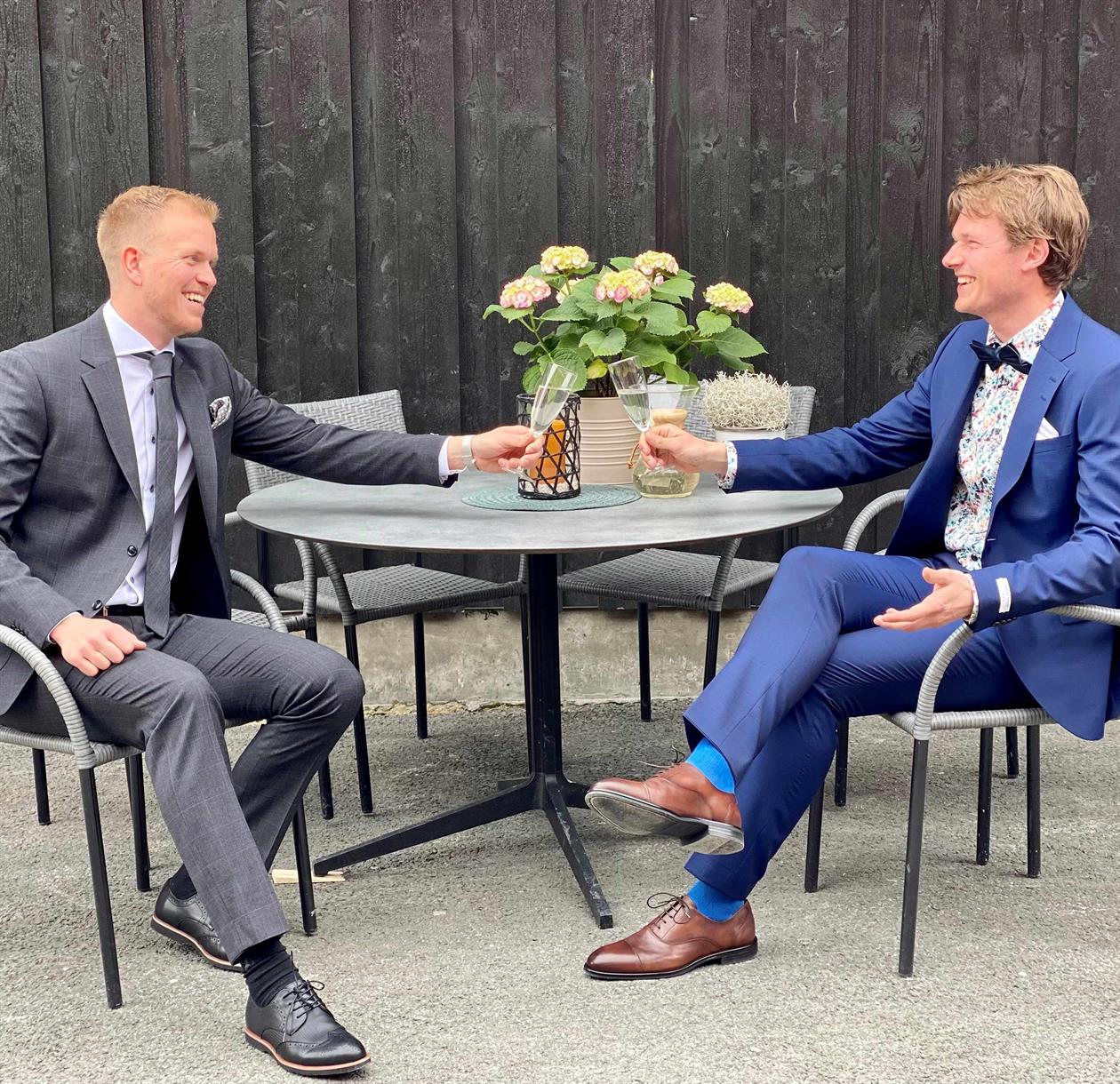 To menn i dress som skåler i champange. Sommer og bryllup.