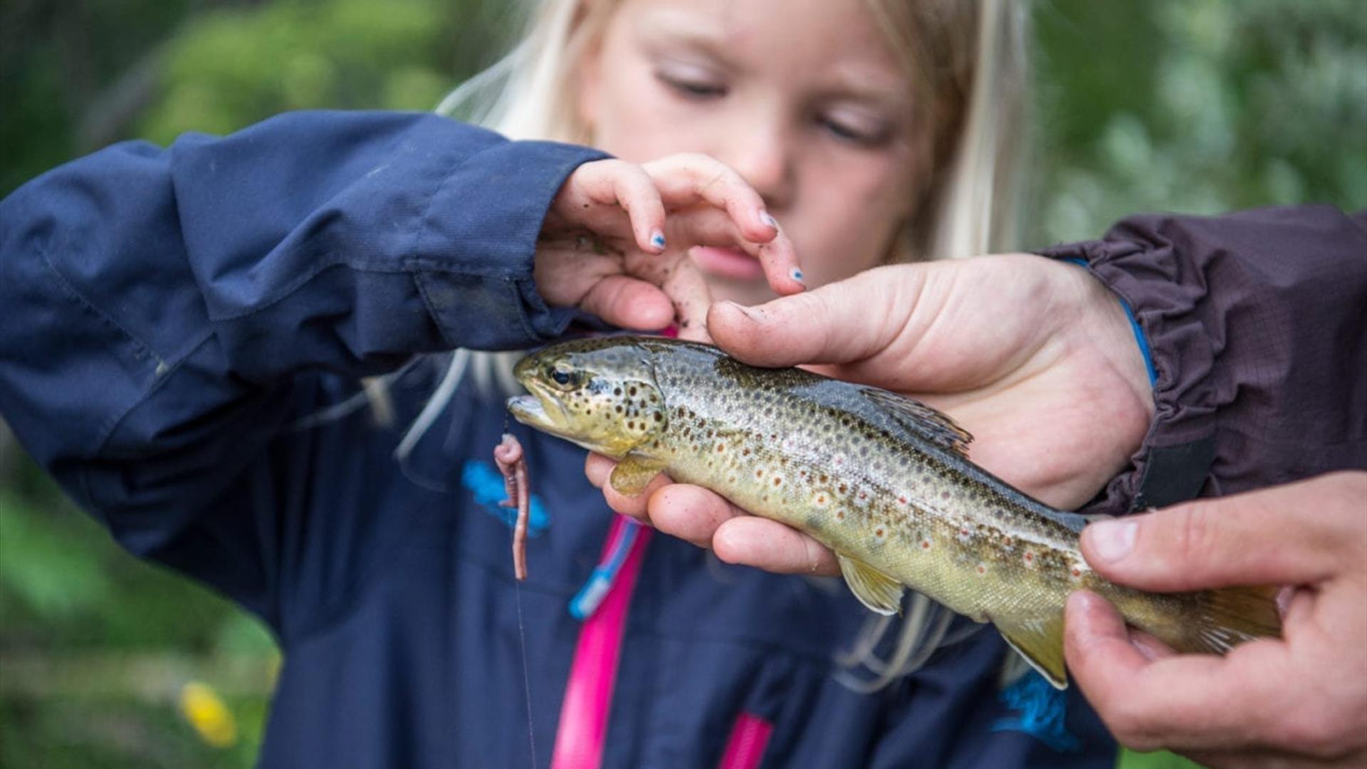 Ei lita jente ser på fisken hun nettopp har fanget