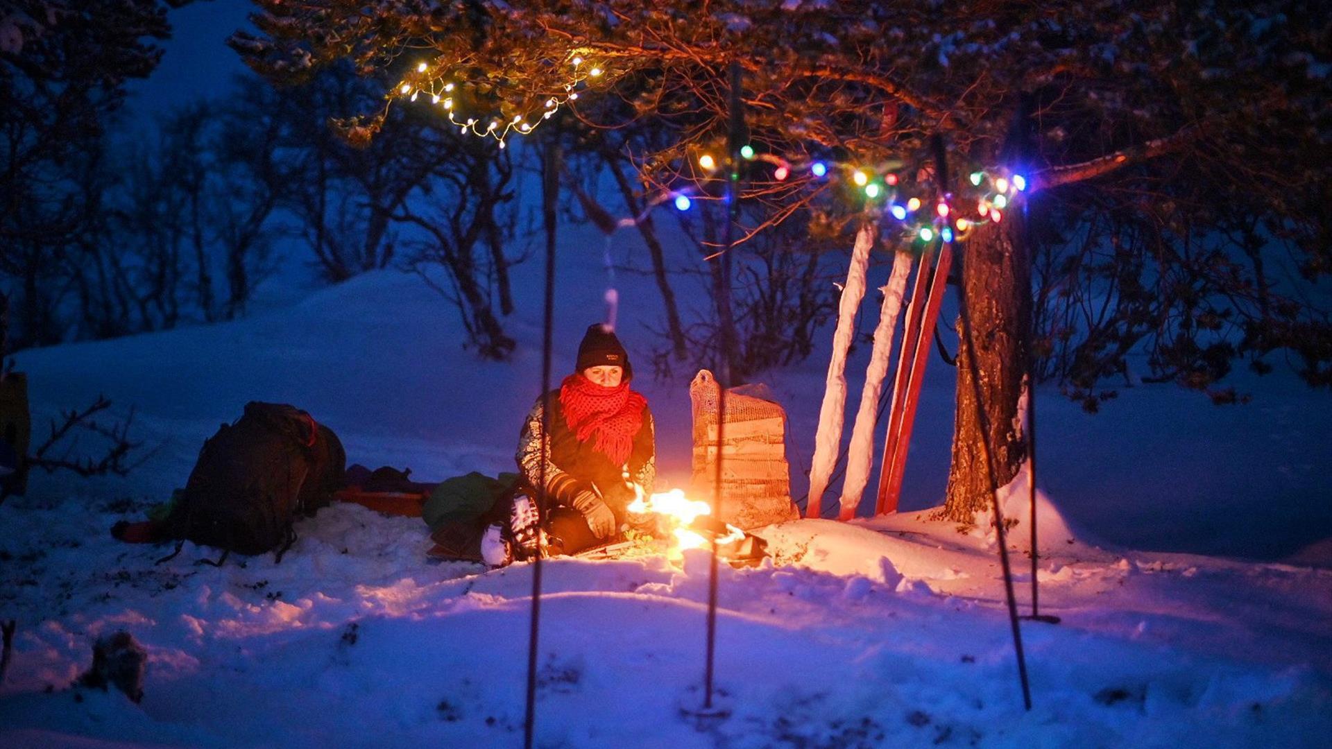 Camping i blåtimen. Stemningsfullt med bål og farga lys som pynt i treet.