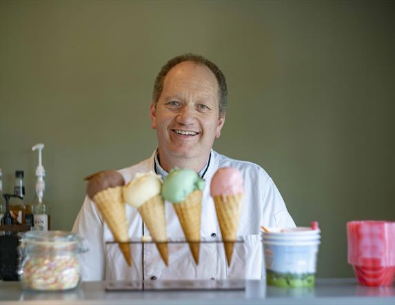 Man smiling standing in front of 4 different ice-creams.