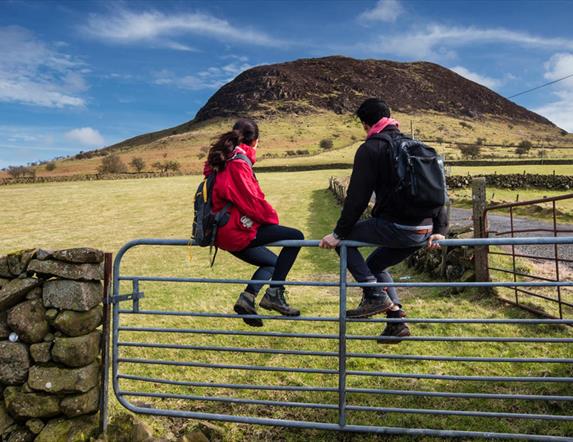 A couple of hikers sitting on a gate admiring the view of Slemish in the background