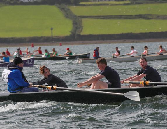 Number of rowers in rowing boats in the sea competing in a race, with shore in background