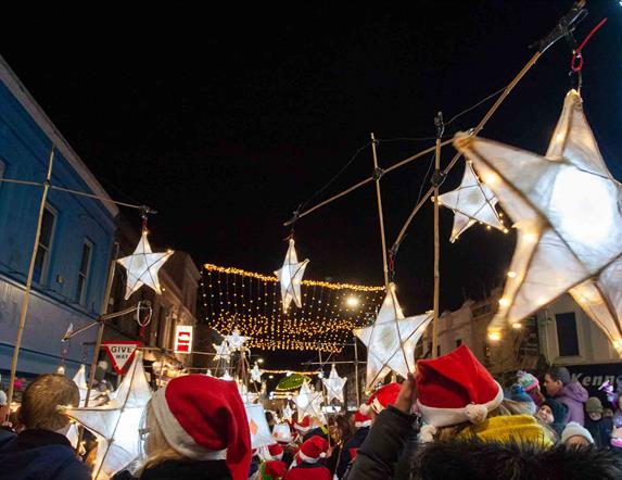 People parading with star lanterns and wearing Santa hats in Ballymena town centre with Christmas lights switched on.