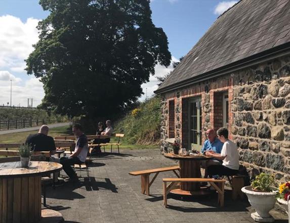 Stone cottage with people dining outside at picnic tables.