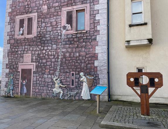 Medieval wall mural in Carrickfergus, with stocks beside it.
