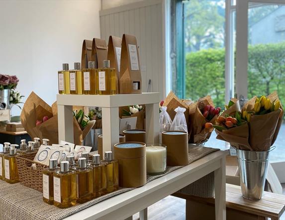 Table display of fragrances and oils with bunches of flowers in bucket displays behind.