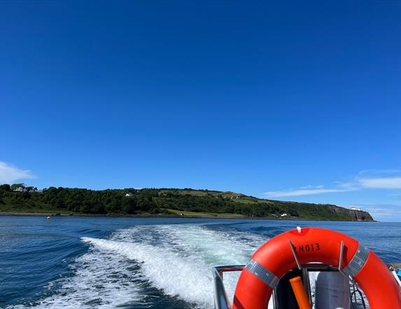 View of Blackhead path and Lighthouse with wake of sea behind boat and life ring visible on Charter NI Boat