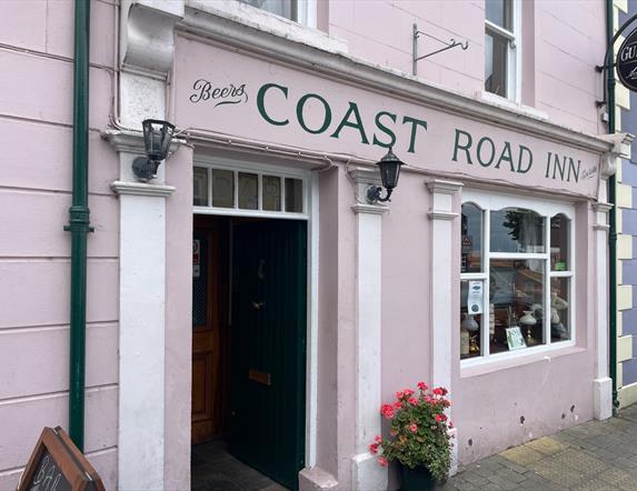 Pink exterior of Coast Road Inn in Glenarm with flowers outside and collectible window display