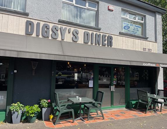 Grey, brown and green exterior of Digsy's Diner with green outdoor seating and plants
