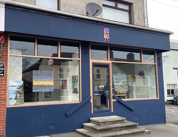 Exterior of the Gallery in Whitehead, painted blue with large windows and art displayed in them