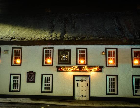 Night time exterior of the Thatch Inn Bar & Restaurant - white building with thatched roof and lights on in the upper windows