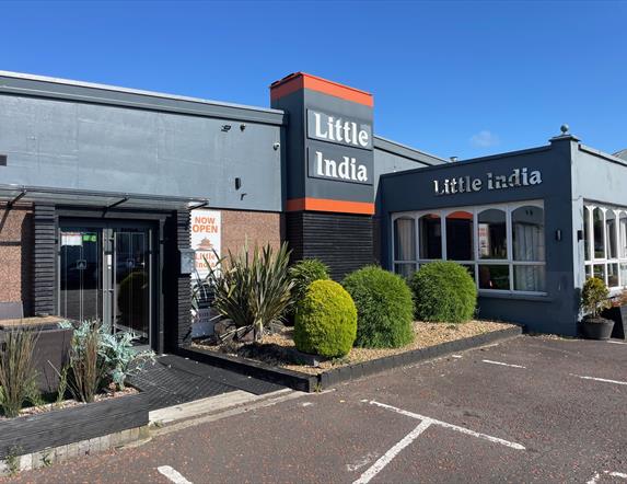 Exterior of Little India Restaurant with grey walls and name in silver, plus plants at the entrance doors