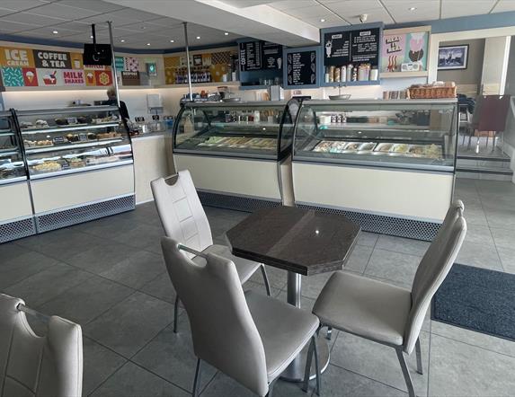 Grey seats and table with ice cream counters and food display fridges in the background