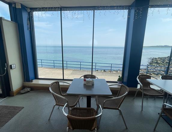Table and seats within Prom Cafe looking out window to sea.